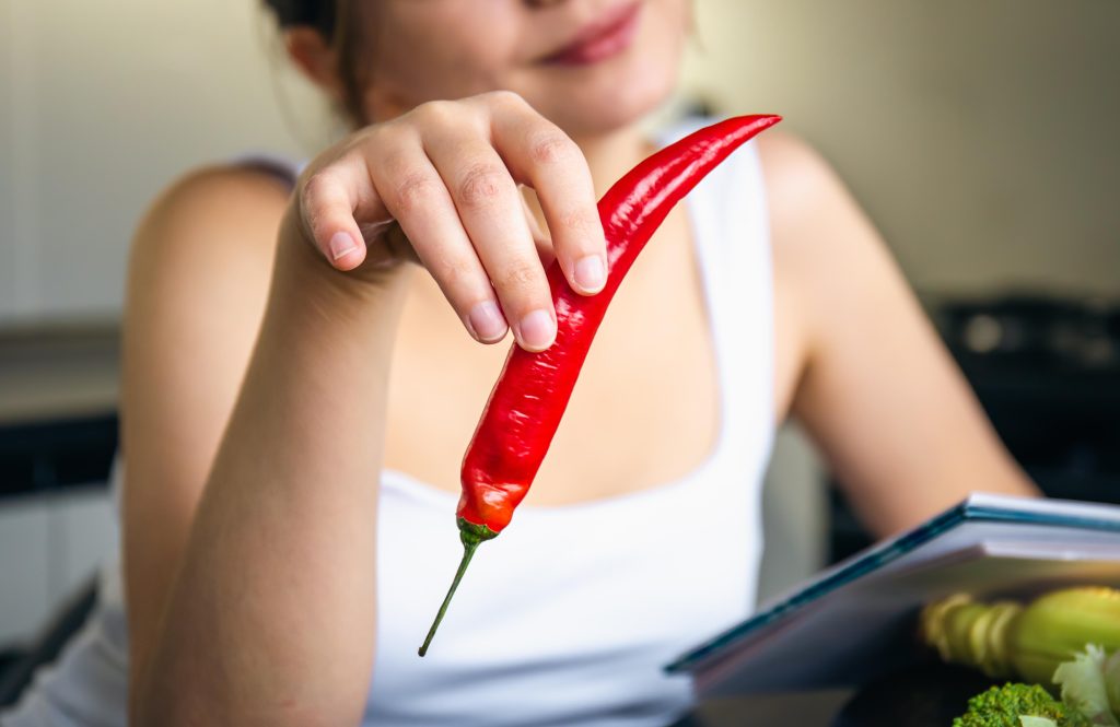 A woman holds a spicy pepper.