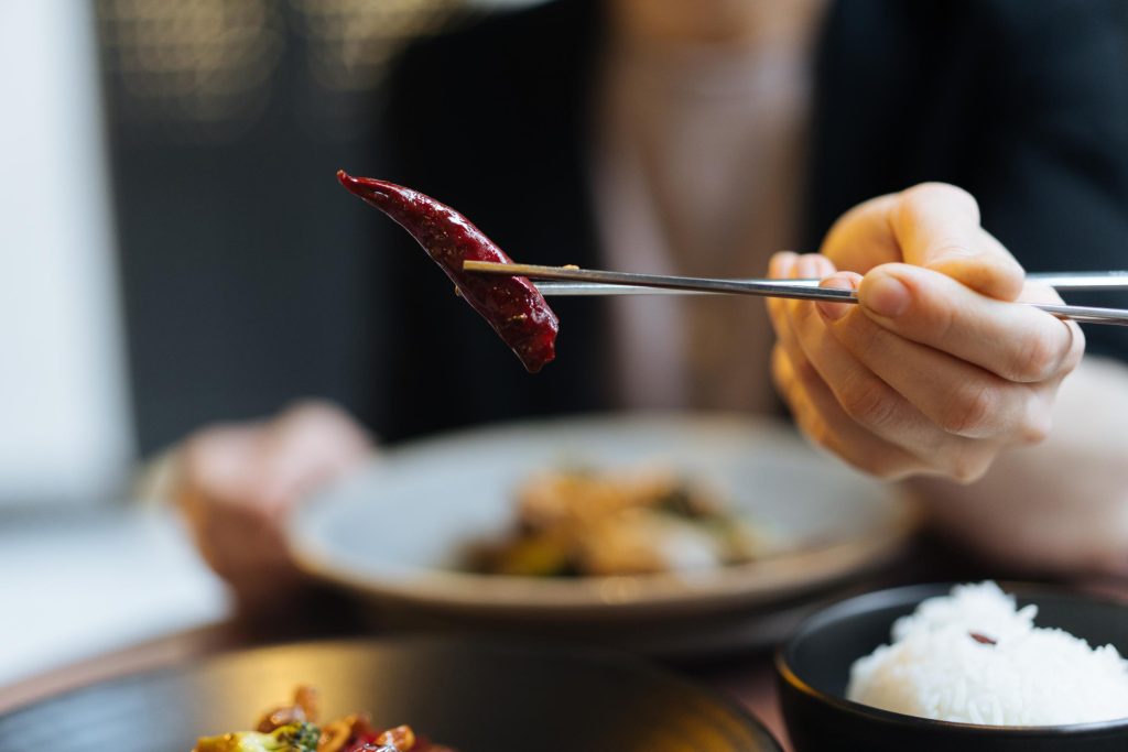 A woman holds a spicy pepper with a pair of chopsticks.